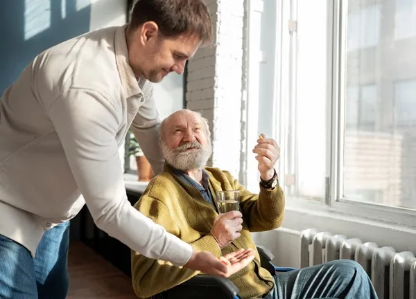 Senior man in wheelchair receiving medication support from caregiver at assisted living community