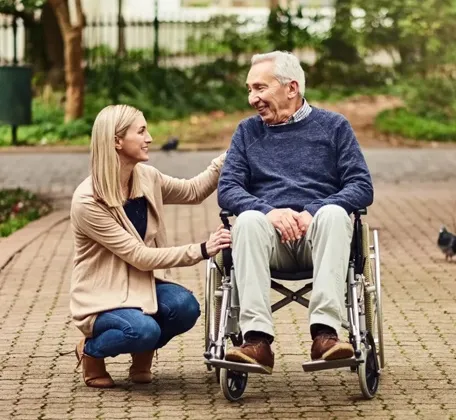 Caregiver assisting senior man in wheelchair during outdoor walk at assisted living community