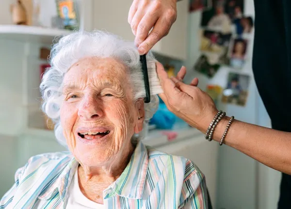Elderly woman receiving personal grooming assistance from a caregiver