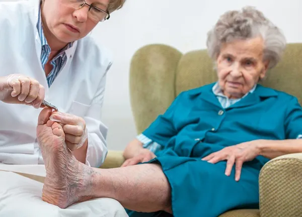 Podiatrist providing nail care to a senior woman in an assisted living community.