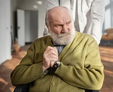 Senior man with Parkinson’s dementia receiving caregiver support in a memory care facility.