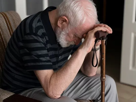 Senior man with Parkinson’s disease sitting with a cane showing mobility challenges
