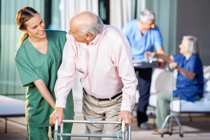 Caregiver assisting elderly man walking with a walker at an assisted living facility
