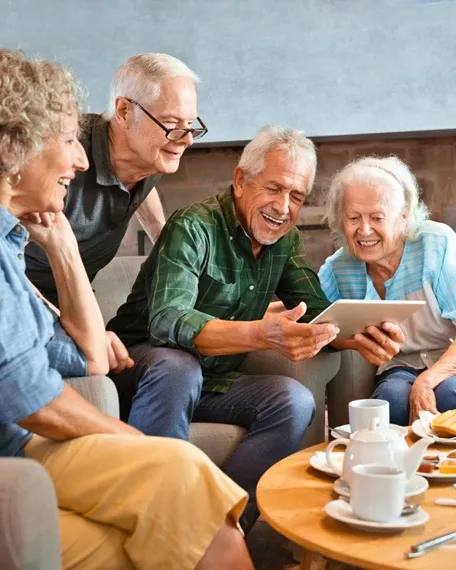 Group of elderly friends enjoying digital entertainment on tablet at senior living home