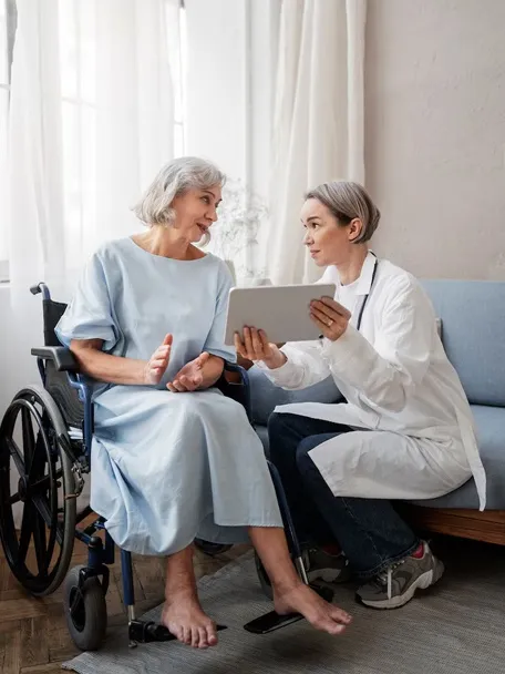 A doctor speaks with an elderly woman in a wheelchair, demonstrating attentive communication in a healthcare environment.