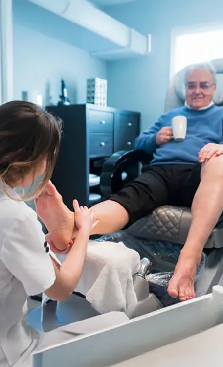 Senior man receiving foot care and pedicure service from caregiver at assisted living facility